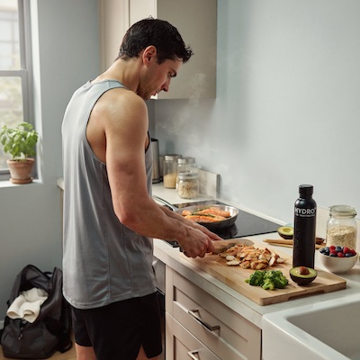 Deportista preparando con tranquilidad una comida sólida rica en proteínas tras su entrenamiento de fuerza
