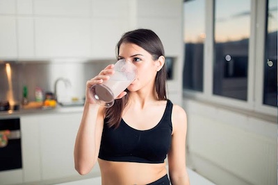 Batido de proteína en polvo Whey Protein junto a una coctelera en el gimnasio